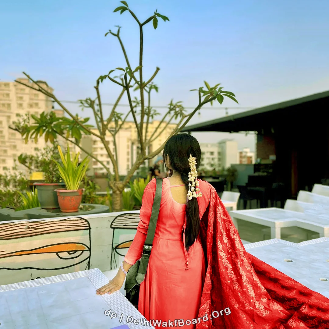 A beautiful girl wearing pink and red tone cloth with a handbag hab. She is standing in a 5-star hotel penthouse showing her beautiful back figure.