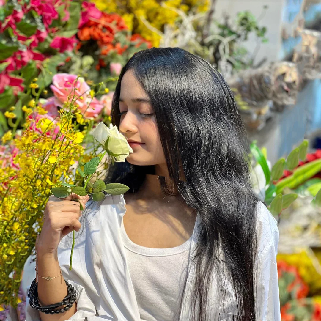 A beautiful young girl surrounded by a variety of colourful flowers and bokeh. She picks a white rose and smells it.